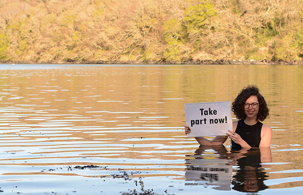 Researcher in River Dart with a sign sayng take part