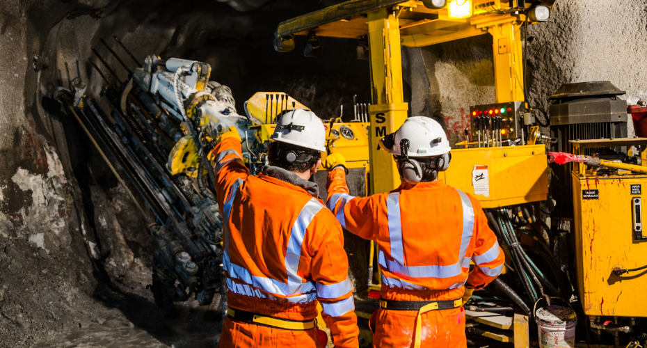 two miners in orange overalls standing next to an excavator