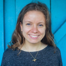 A female student smiling standing in front of a blue wooden door