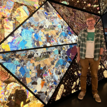 A male student standing in front of a stained glass window