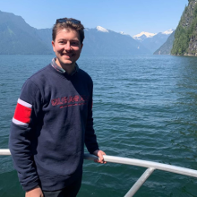 A student standing on boat with mountains in the background