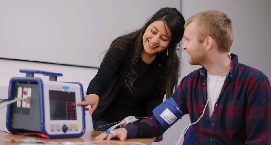 A Psychology academic demonstrating a blood pressure machine to a participant in an experiment