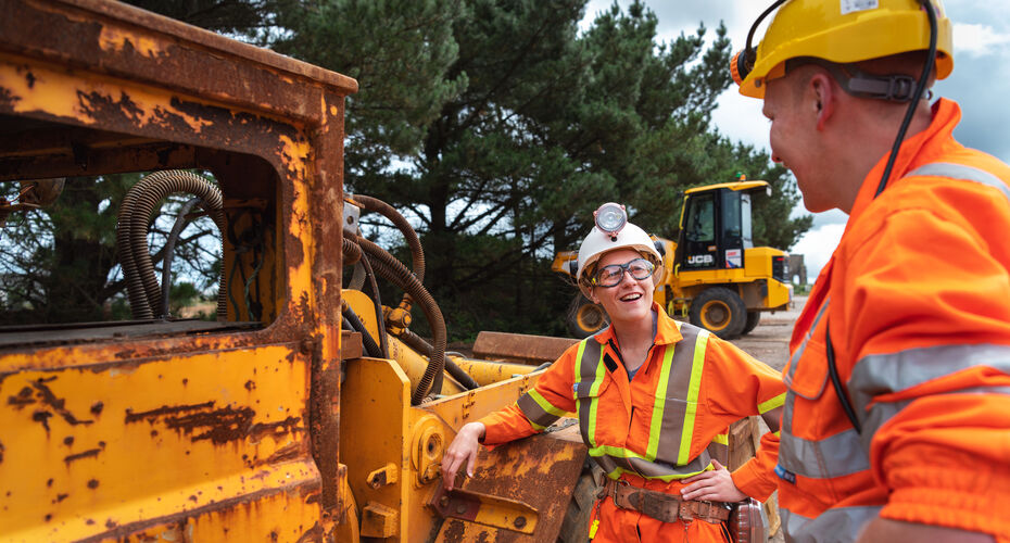 Two people in hi-vis clothing in conversation next to mining machinery