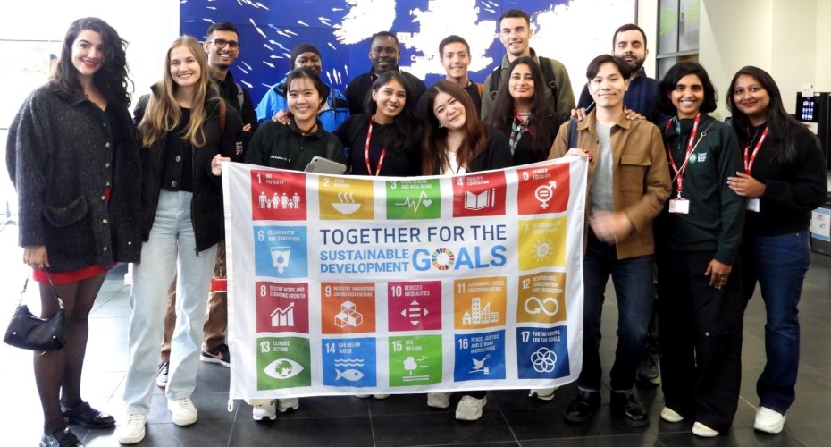 A group of exeter mba students at the met office holding a banner that reads together for the goals promoting sustainability.