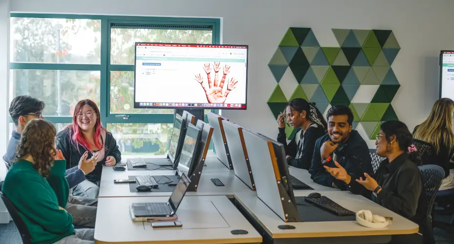 Group of six students working together in computer science lab with a display monitor overhead