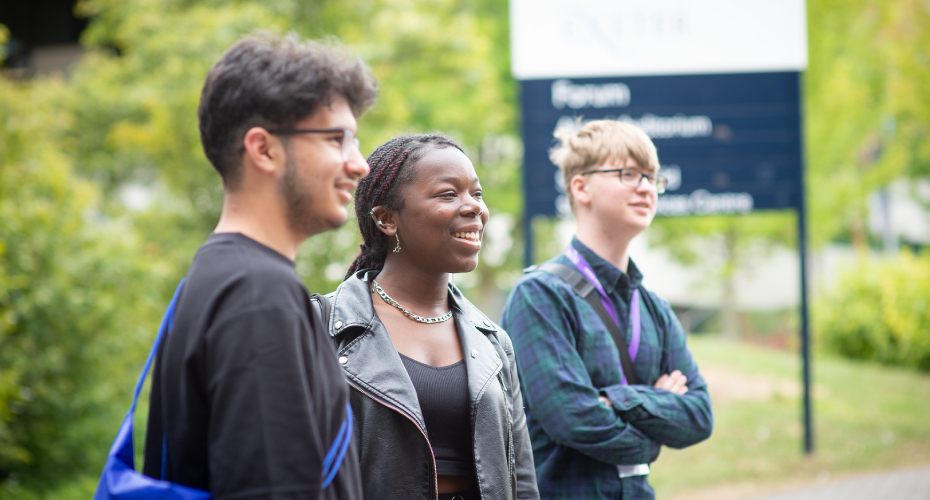 Three students on Streatham campus, in front of forum sign