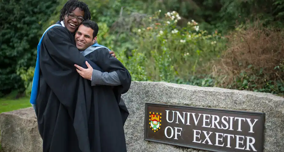 Two friends embrace by the University of Exeter rock at winter graduation