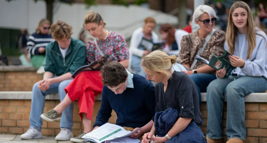 Prospective students and their families sat at the Forum on Streatham Campus, reading a University handbook.