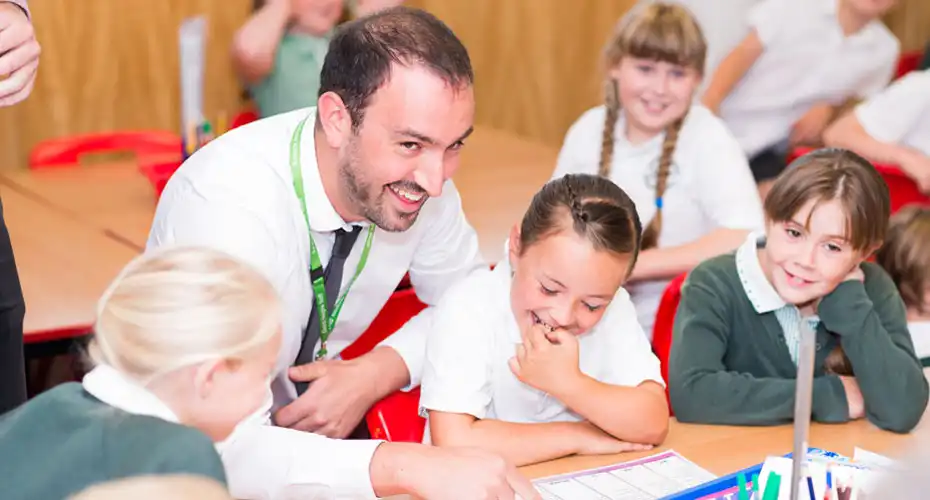 A male primary school trainee teacher delivering a fun and interactive lesson in a classroom