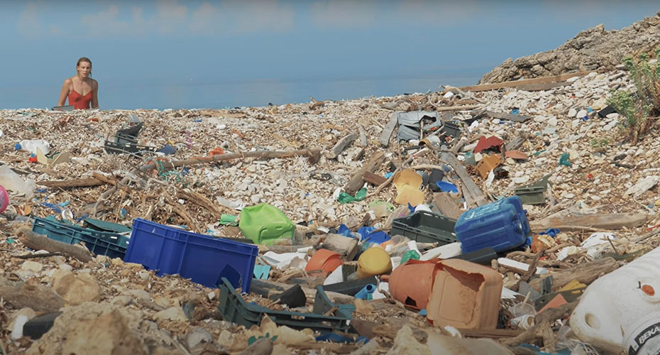 A woman stands on a beach littered with trash and plastic, highlighting environmental pollution and its impact on nature.