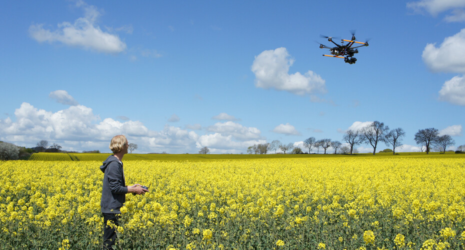 A man standing in a field with a drone flying over him.