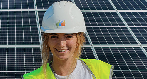 Lady in hard hat in front of solar panel.