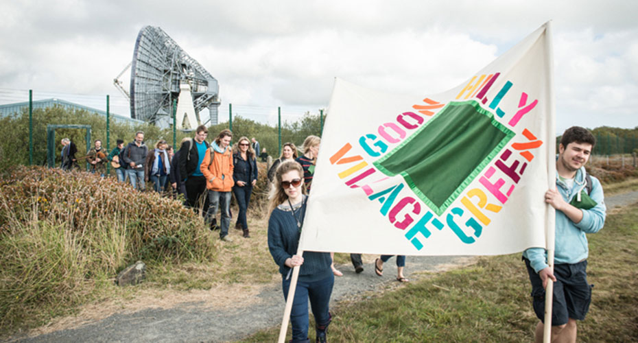 A group of people walking outdoors, led by two individuals carrying a large banner that reads 