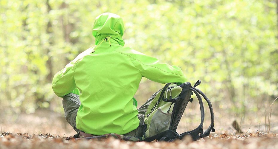 Person sitting on ground in forest location wearing wet weather gear