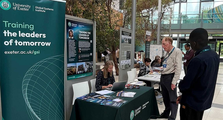 A group of individuals gathered around a table displaying a poster, engaged in discussion and collaboration.