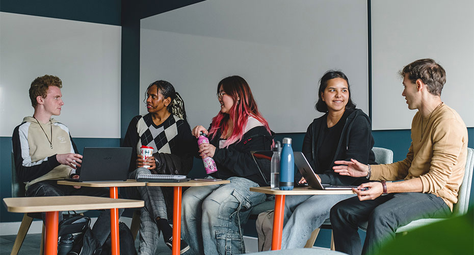 A diverse group of students collaborates at a table, each using their laptops for a study session.