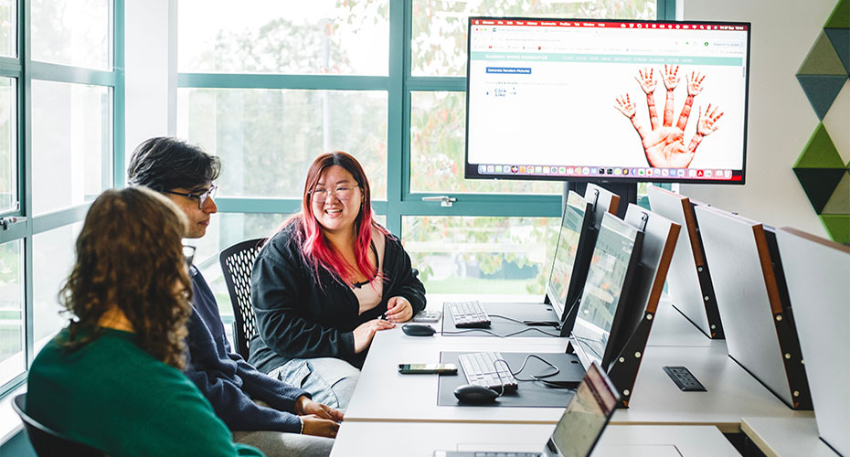 A group of three people gathered around a table, engaging with a computer screen in front of them.