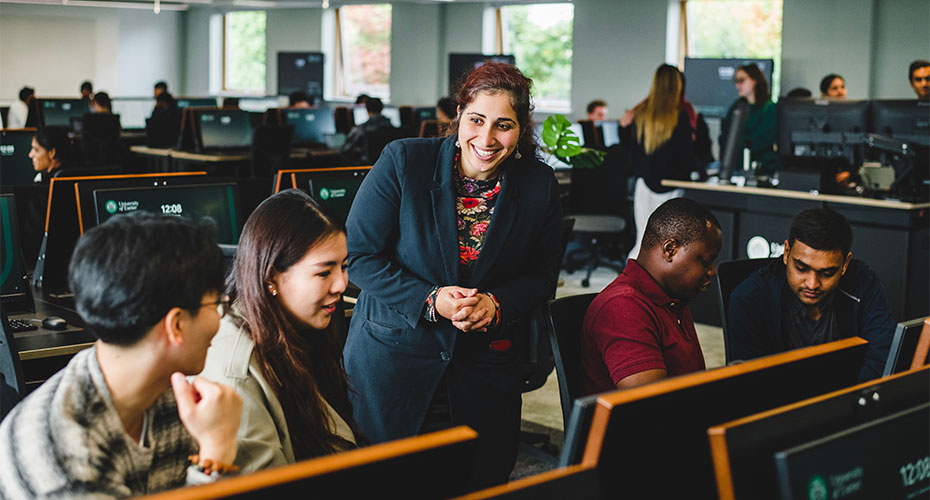 A woman smiles while engaging with students in a computer lab, fostering a positive learning environment.