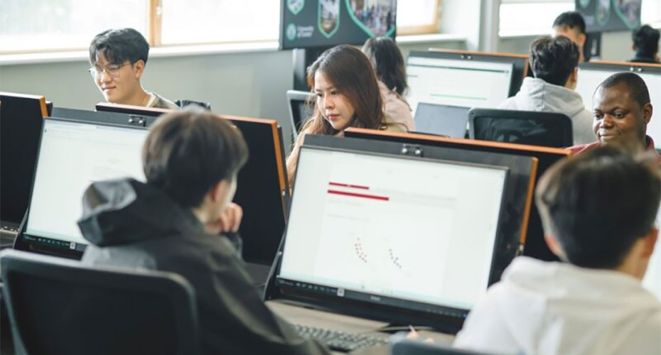 A group of students collaborating on computers in a classroom setting, focused on their tasks and engaged in learning.