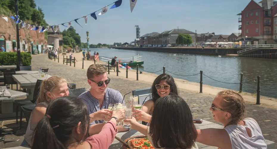 Study Abroad students who have come to the University of Exeter eating pizza by the River Exe.