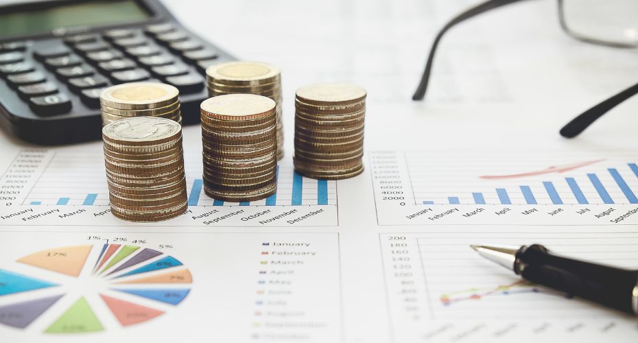 A calculator, some glasses, some stacks of coins, a pen, and prints of various graphs and a pie chart.