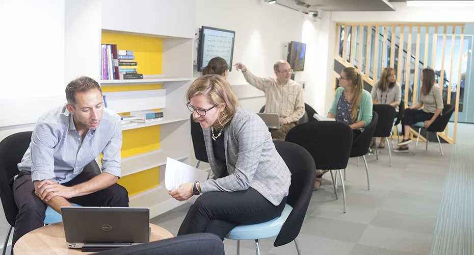 An image of groups of people working on laptops and display screens in the breakout space