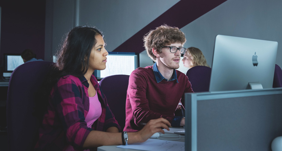 Two individuals collaborating on computers in a modern office setting, focused on their tasks.