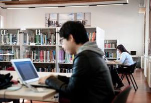 A group of students studying together in a library, surrounded by books and focused on their work.