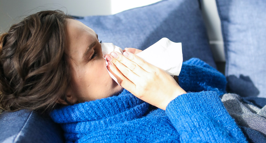 Womanin blue jumper blowing nose on bed