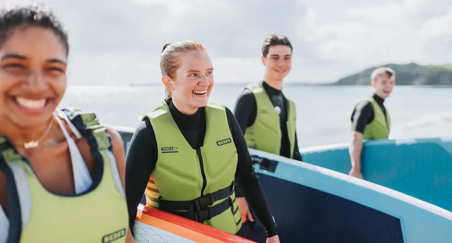 Group of students holding surfboards and wearing wetsuits, laughing