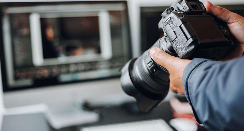 Person holding  a camera in their hands in front of a laptop.