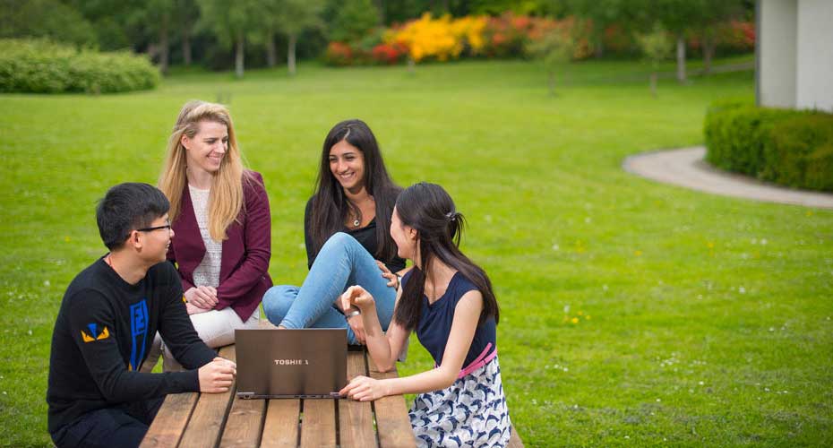 Four students seated on a bench in a park, engaged in conversation amidst a serene outdoor setting.