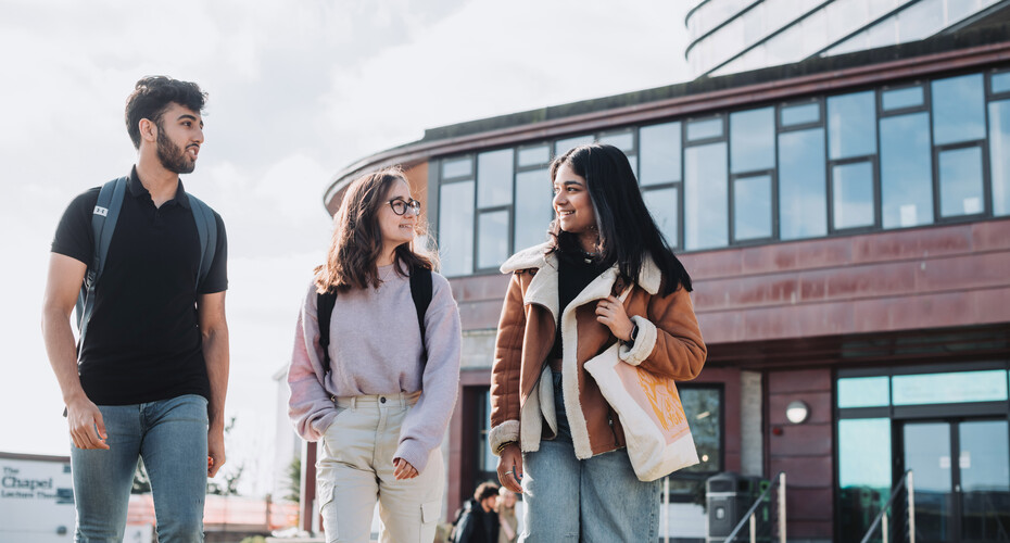 Three students walking outside The Stannary Bar building, Penryn Campus